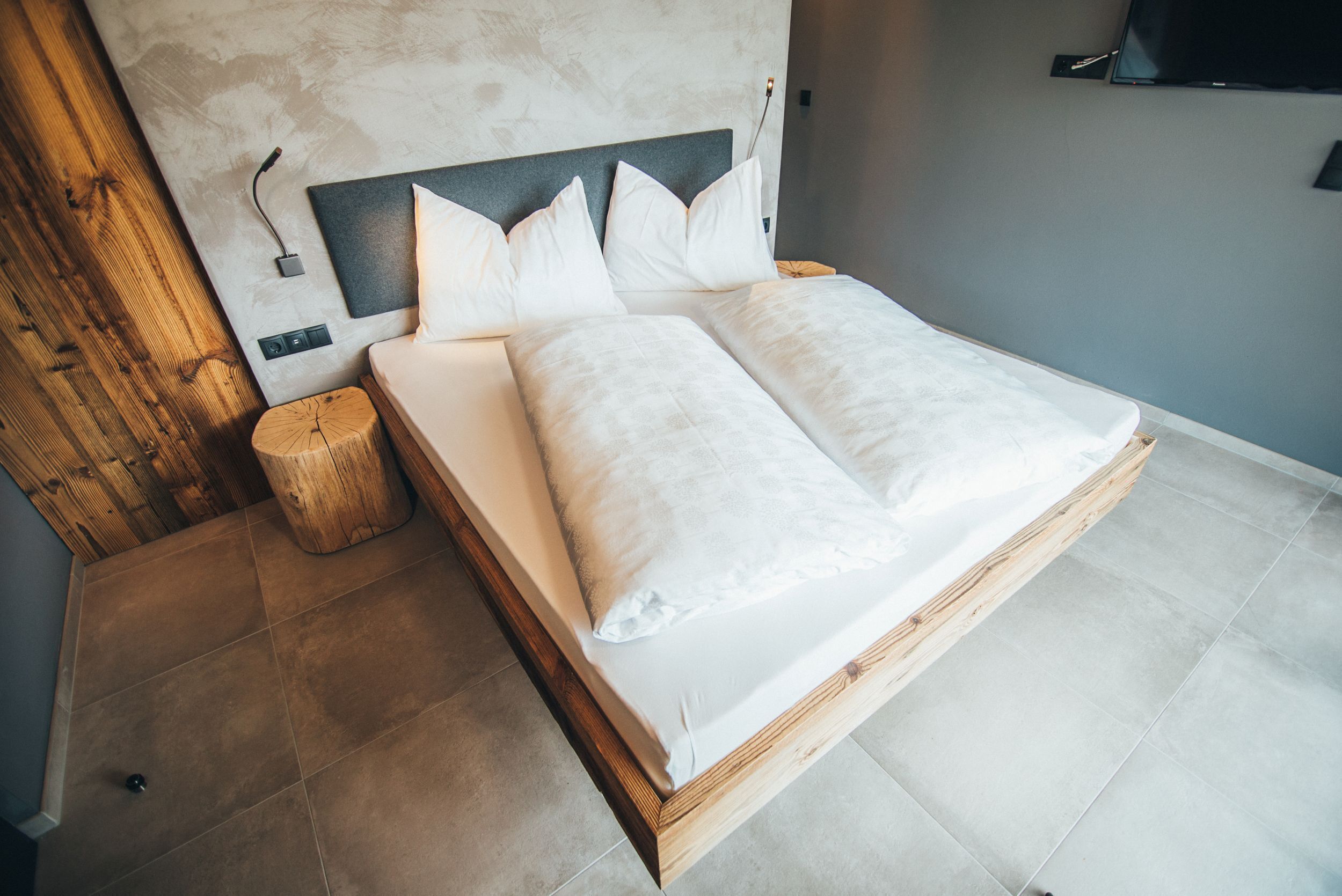Een moderne slaapkamer met een houten hoofdbord, een nachtkastje van hout en een groot bed met witte beddengoed.