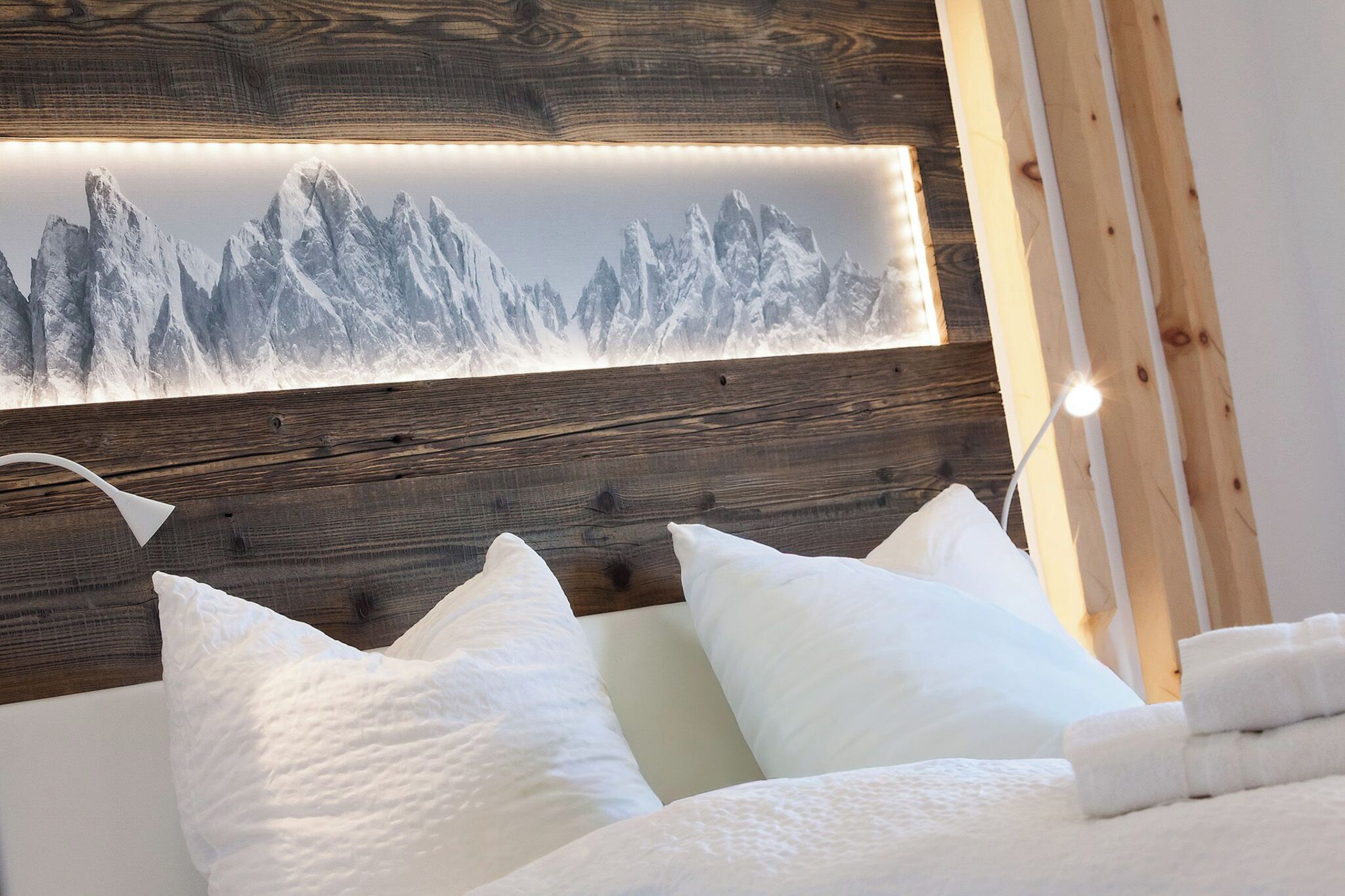 A bedroom with a wooden headboard, white pillows, and a framed mountain landscape picture.