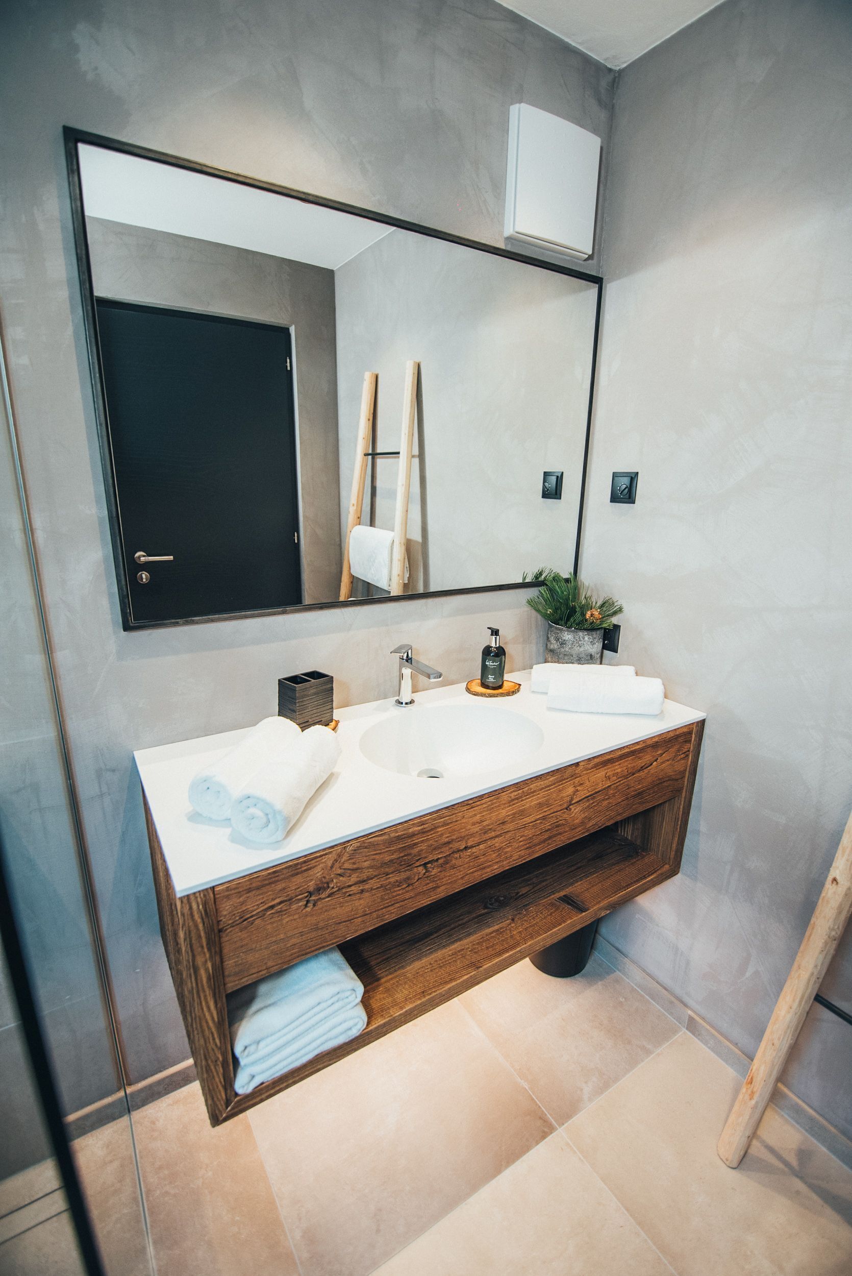 A modern bathroom with a large mirror, a wooden vanity, a white sink, and a towel rack.