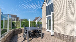 An outdoor patio with a table and chairs, a brick wall, and a glass door. - Charming Villa Near the sea and Forest (De Koog)