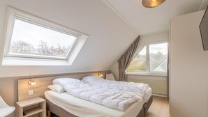 A bedroom with a large bed, a nightstand, a desk, and a window with curtains. - Charming Villa Near the sea and Forest (De Koog)