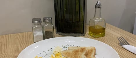 A plate of scrambled eggs, toast, and a small bottle of oil on a wooden table.