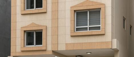A multi-story building with a beige facade, multiple windows with white frames, a glass staircase, and a metal gate.