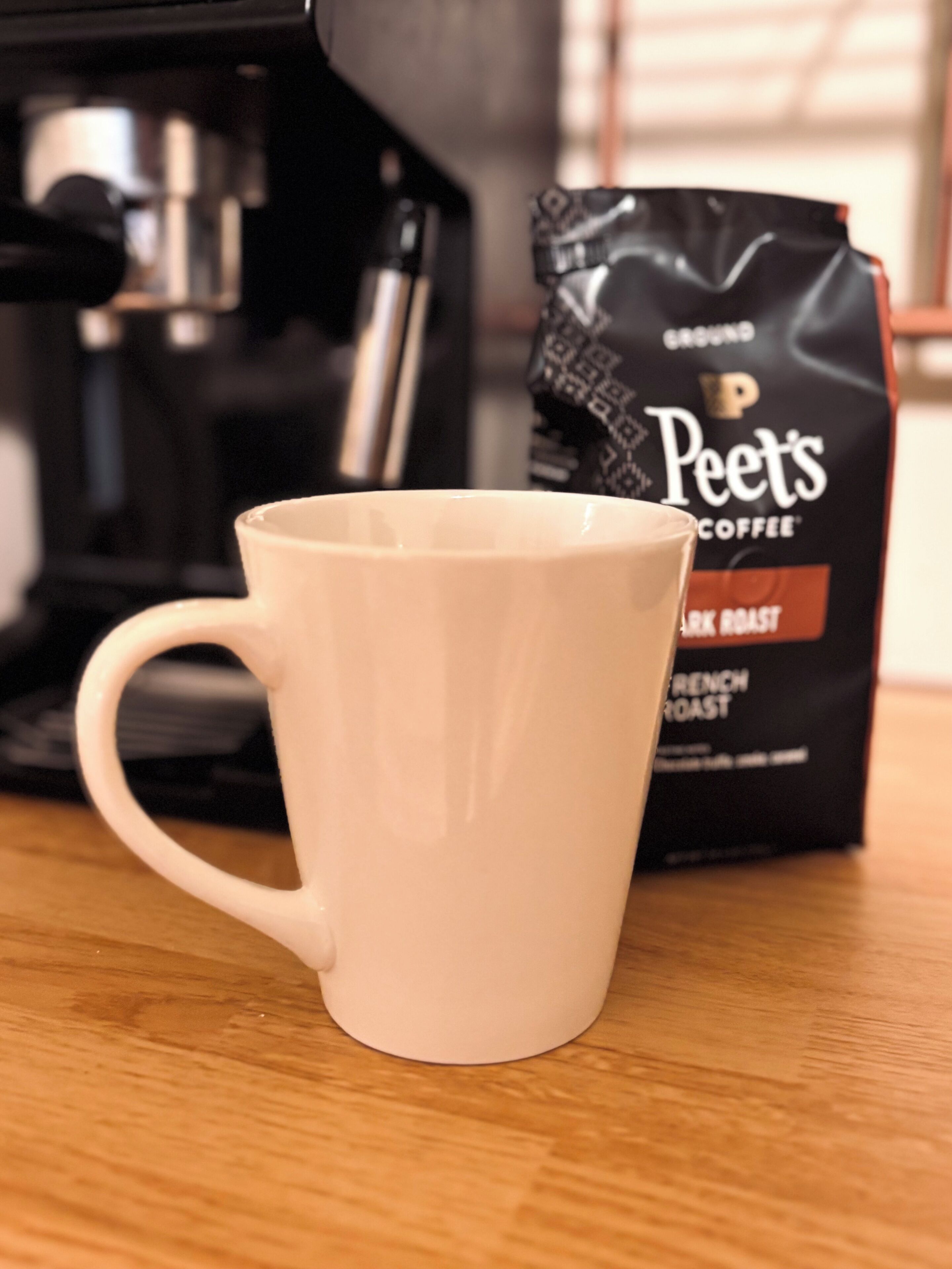 Una taza blanca sobre una superficie de madera, con un paquete de Peet's Coffee al fondo.