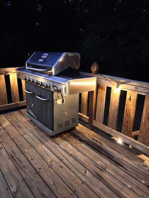 A stainless steel barbecue grill on a wooden deck with a railing.