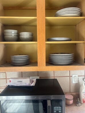 A kitchen with wooden shelves holding plates and bowls, a microwave, and a small refrigerator.
