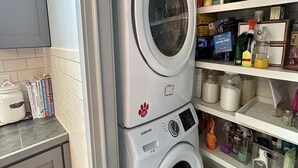 A laundry area with stacked washing machines, a shelf with cleaning supplies, and a tiled floor. - Harvey Cedars Home Designed for your Vacation! (Harvey Cedars)