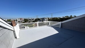 A rooftop terrace with a white railing, a clear sky, and residential buildings in the background. - Harvey Cedars Home Designed for your Vacation! (Harvey Cedars)