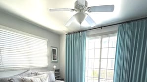 A bedroom with a bed, a ceiling fan, a window with curtains, and a view outside.