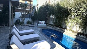 A pool area with lounge chairs, a stone patio, and a building in the background. - Harvey Cedars Home Designed for your Vacation! (Harvey Cedars)