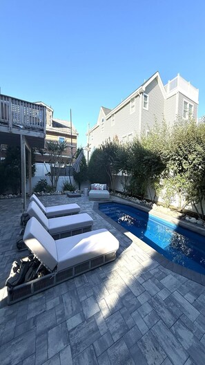 A pool area with lounge chairs, a stone patio, and a building in the background.