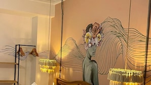 A hotel room with a large bed, a wooden headboard, a wall-mounted lamp, a small table with a chair, and a painting on the wall. - KIM  (Cartagena)