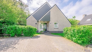 A two-story house with a brick exterior, a grey roof, and a paved driveway leading to a glass door entrance. - Charming Villa Near the sea and Forest (De Koog)