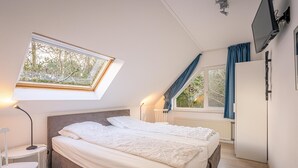 A bedroom with two beds, a skylight, a TV, and a window with curtains. - Charming Villa Near the sea and Forest (De Koog)