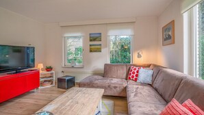 A modern living room with a red entertainment unit, a large flat-screen TV, a brown sectional sofa, and a wooden coffee table. - Charming Villa Near the sea and Forest (De Koog)