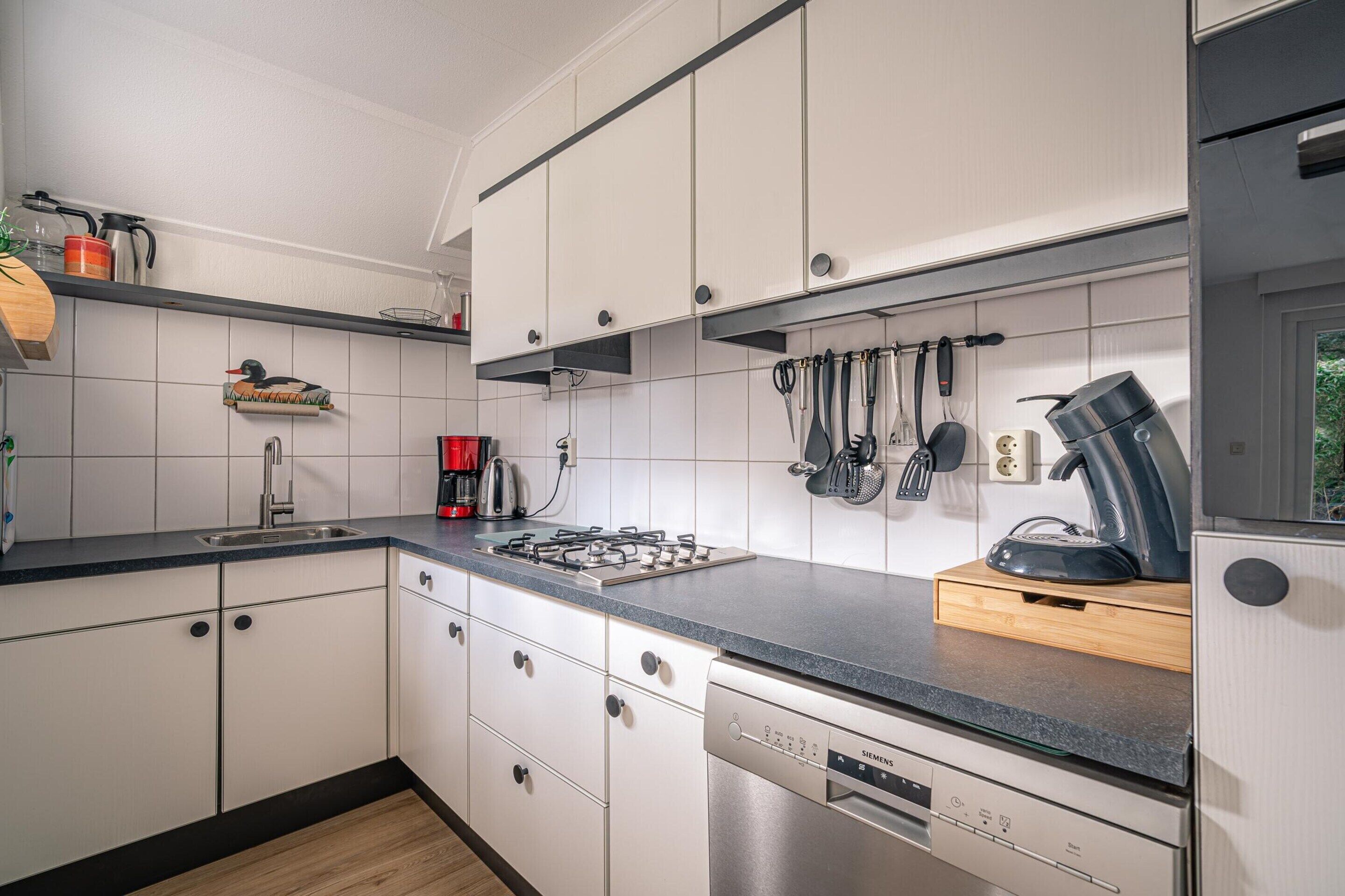 A modern kitchen with white cabinets, a stainless steel dishwasher, and a black countertop.