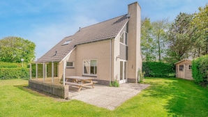 A two-story house with a covered patio and a wooden table. - Charming Villa Near the sea and Forest (De Koog)