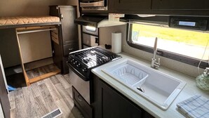 Cocina compacta para autocaravana con estufa, microondas, fregadero y ventana con vistas.