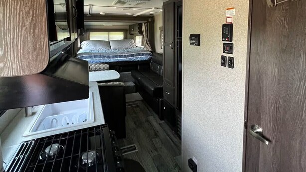 Interior compacto de una autocaravana con kitchenette, cama y baño.