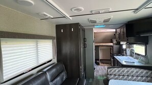 Interior compacto de una autocaravana con kitchenette, comedor y zona de estar con sofá y mesa.