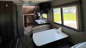 Interior compacto de una caravana con kitchenette, comedor y litera.