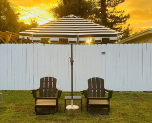 A patio area with two Adirondack chairs and a striped umbrella.