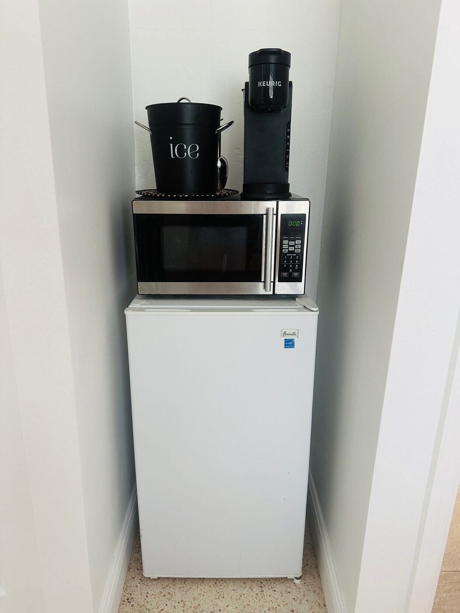 A compact kitchen with a white refrigerator, a microwave, and a coffee maker on top.