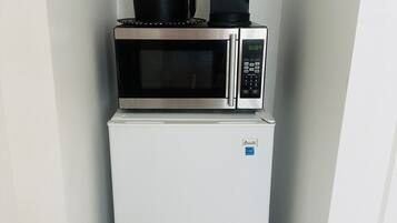 A compact kitchen with a white refrigerator, a microwave, and a coffee maker on top.