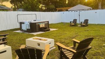A backyard with a hot tub, outdoor seating, and a fire pit.