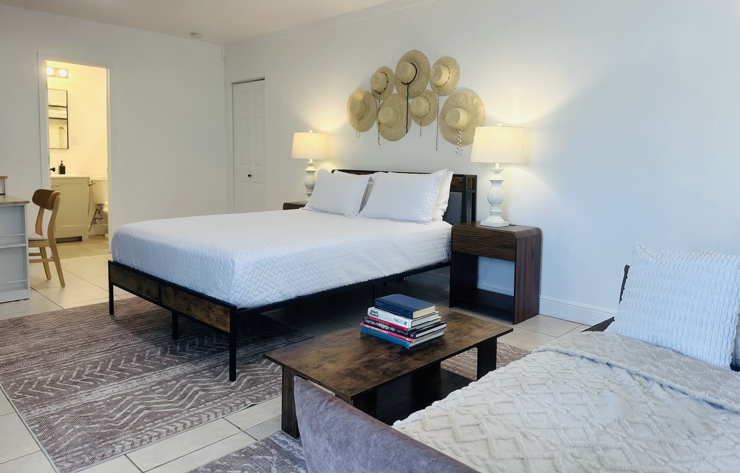 Un dormitorio con cama, mesitas de noche, una mesa de centro y un adorno de sombrero en la pared.