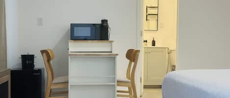 A compact room with a bed, a small kitchenette with a microwave, a coffee maker, and a cabinet.