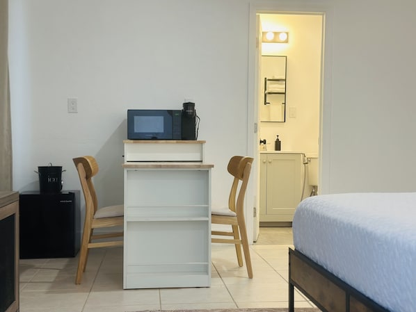A compact room with a bed, a small kitchenette with a microwave, a coffee maker, and a cabinet.