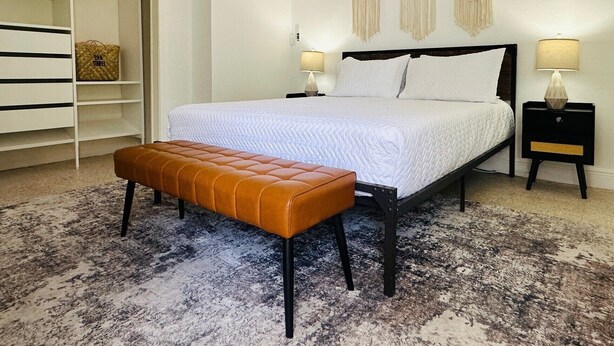 Une chambre à coucher comprenant un lit, un banc, une table de chevet, une lampe, une armoire et des décorations murales en macramé.