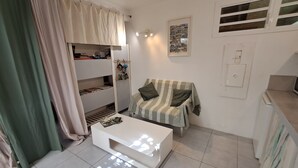 A small, well-lit room with a bunk bed, a striped sofa, a white coffee table, and a wall-mounted picture.