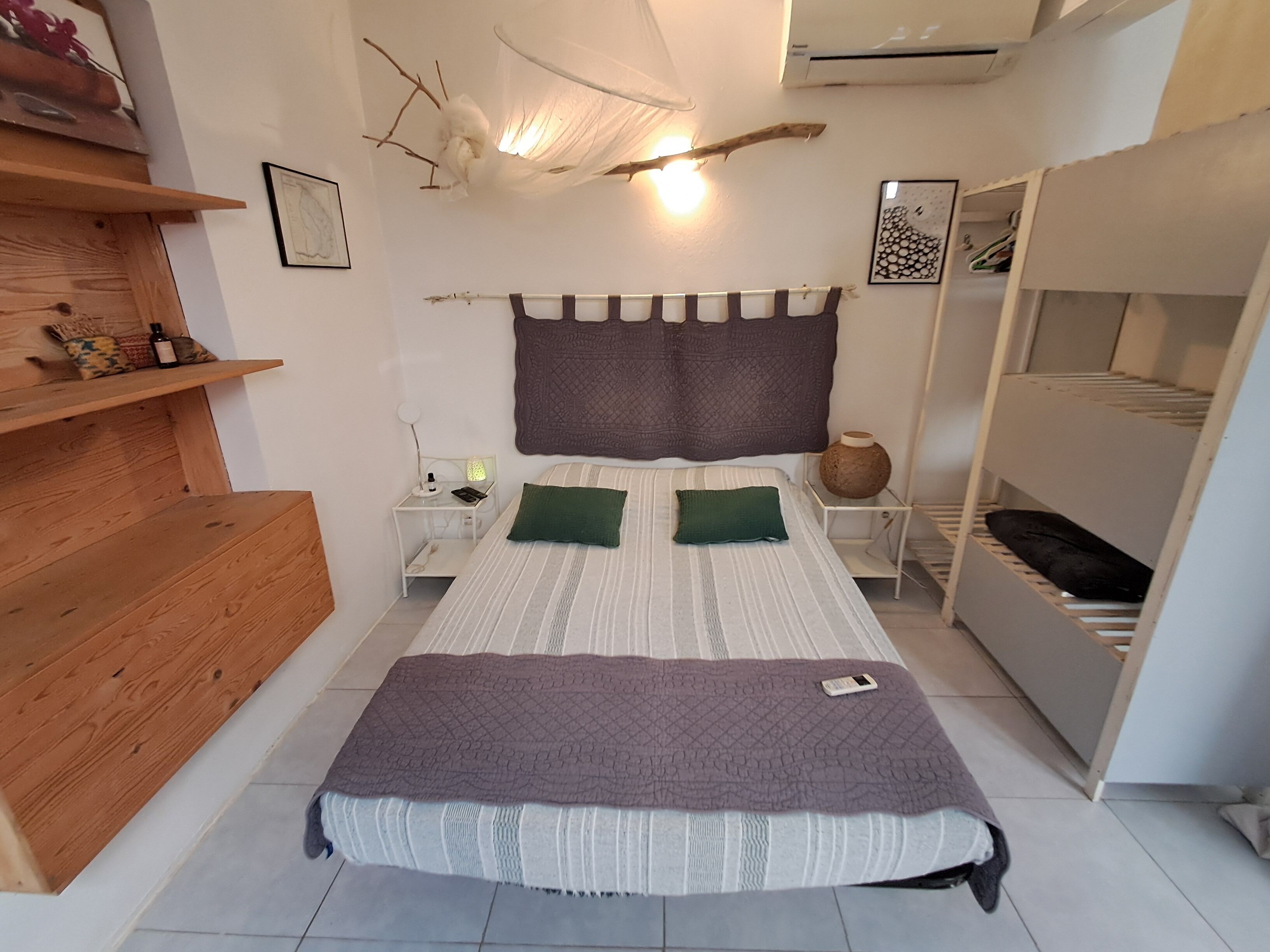 A bedroom with a bed, bedside tables, a nightstand, a shelf, a wardrobe, and a hanging light fixture.