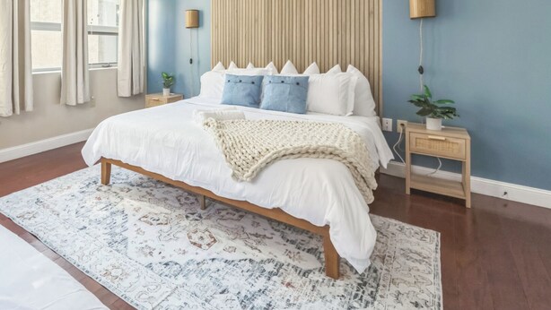 Un dormitorio con una cama grande, un cabecero de madera, un tapete estampado y una mesita de noche con una lámpara.