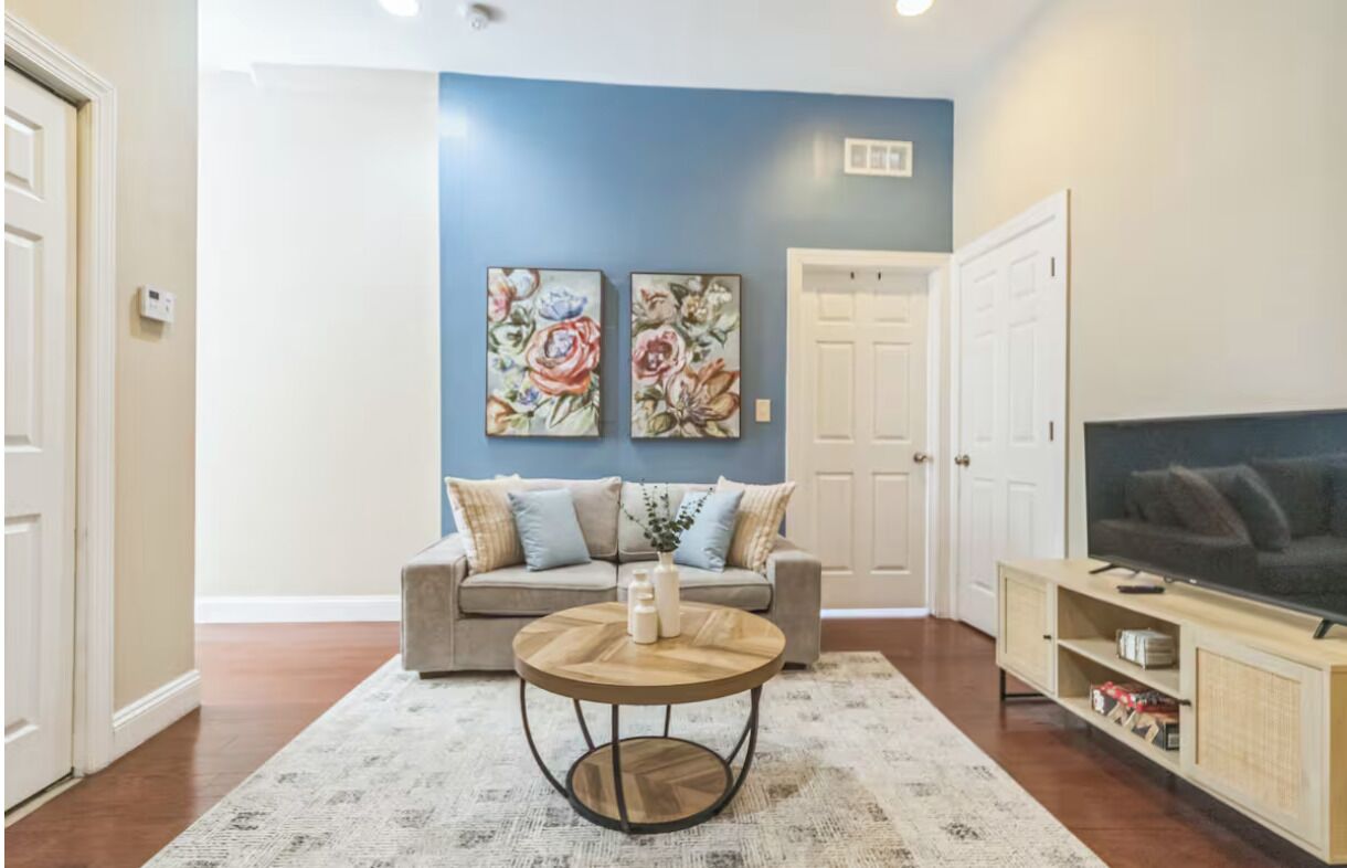 A living room with a sofa, a coffee table, a TV, and two floral paintings on the wall.