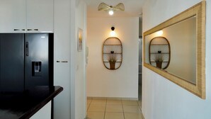 Un couloir comprenant un réfrigérateur, un luminaire fixé au mur et un élément décoratif encadré.