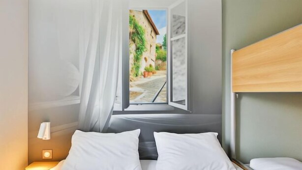 A bedroom with a bed, a nightstand, a window with a view of a street, and a headboard. - B&B Hotel Valence Sud (Valence)