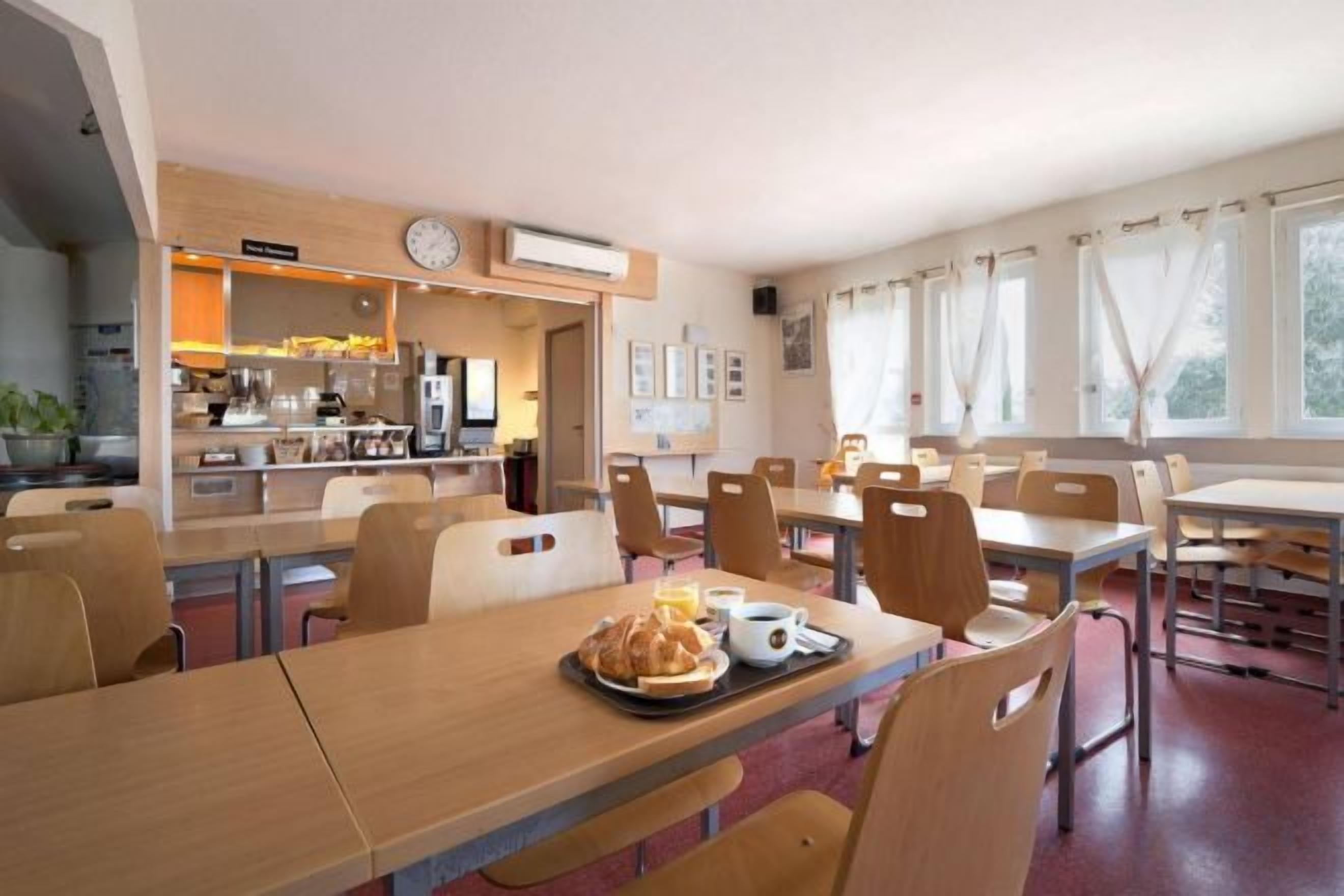 A dining area with multiple tables and chairs, a kitchen in the background, and a clock on the wall.
