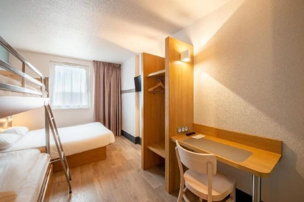 A compact hotel room with bunk beds, a desk, and a shower area.