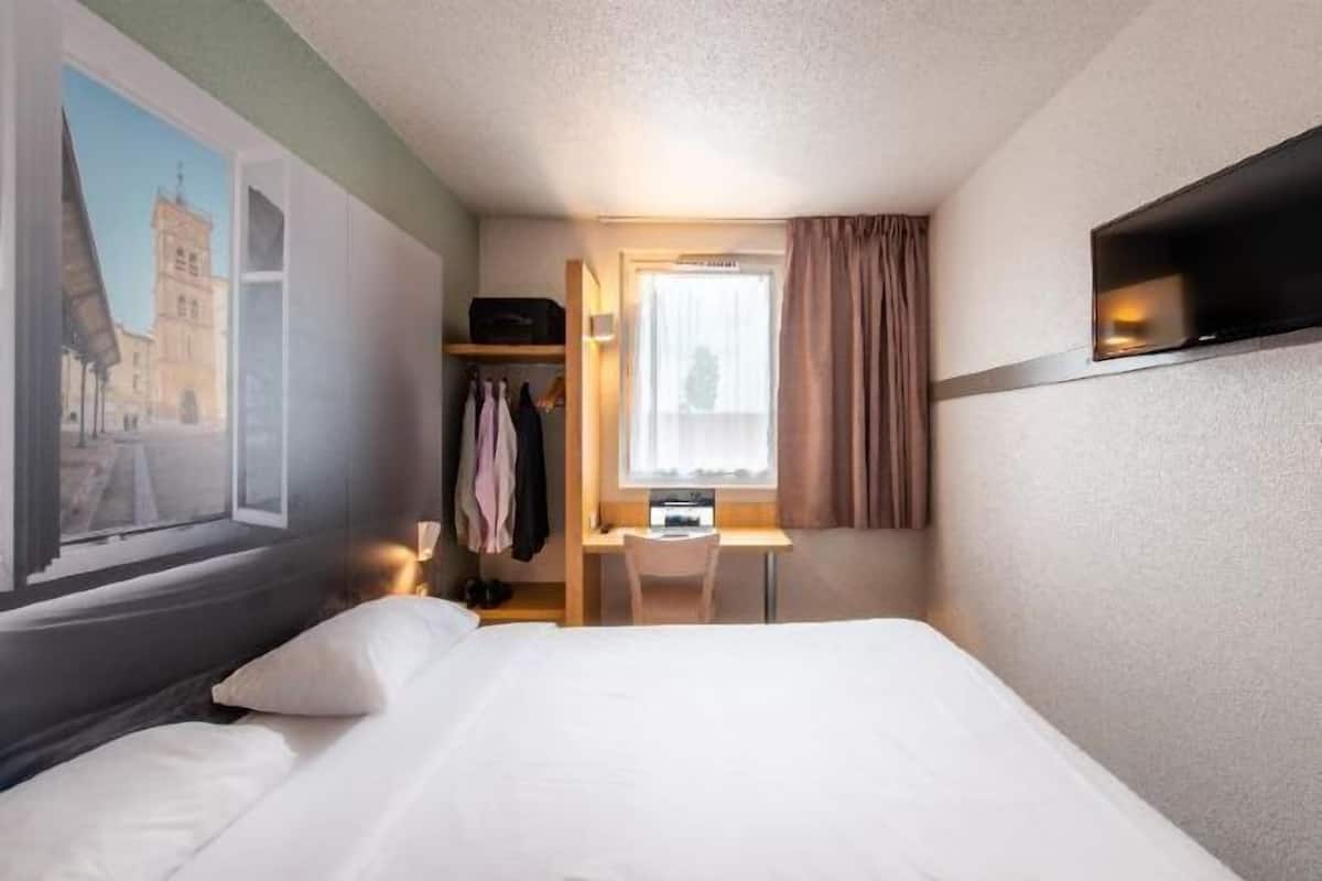 A hotel room with a bed, a desk, a chair, a TV, and a window with curtains.