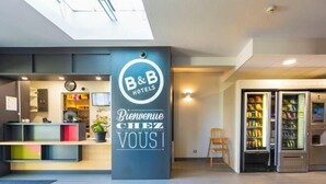 A B&B hotel reception area with a modern design, a welcome sign, a reception desk, a clock, and vending machines. - B&B Hotel Valence Sud (Valence)