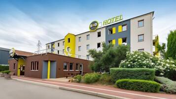 Een hotel met een geel-witte gevel, meerdere verdiepingen en een goed onderhouden tuin.
