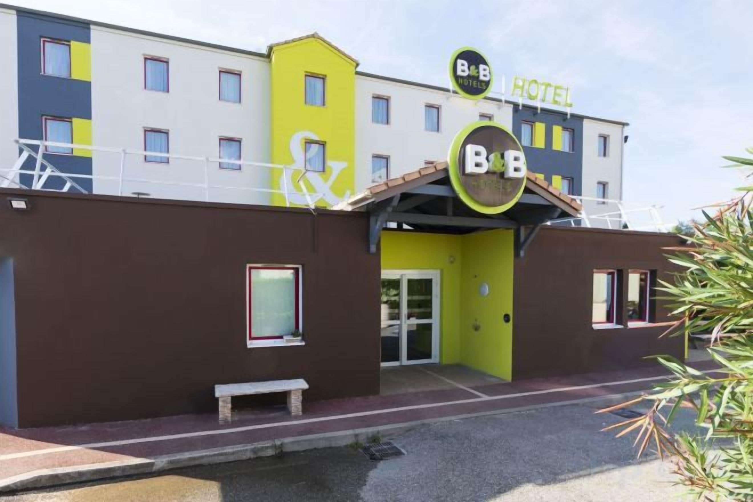 A hotel with a distinctive B&B sign, a covered entrance, and a small bench outside.