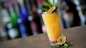 Een hoog glas met een geel drankje, versierd met een blaadje en een stuk fruit, op een barkruk.