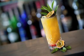Un vaso alto con una bebida amarilla, decorado con una hoja y una rodaja de fruta, sobre una barra.