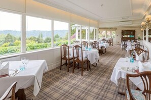 A dining area with tables set for service, large windows offering a view of greenery, and a checkered floor pattern. - Lindeth Fell Country House (Bowness-on-Windermere)