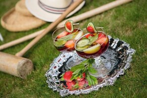 Dos vasos de una bebida de frutas sobre una bandeja de plata con fresas y hojas de menta, sobre césped.