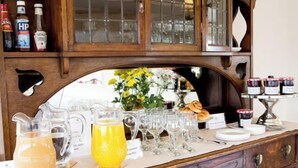 Montaje de un bufé de desayuno con diversas bebidas y alimentos, incluyendo una jarra de jugo de naranja y una variedad de condimentos en los estantes.